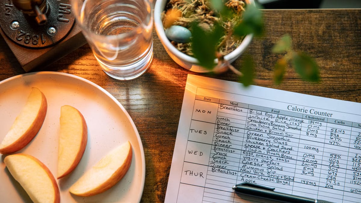 Top view of apple slices, water, and a calorie counter sheet on a wooden table promoting a healthy lifestyle.